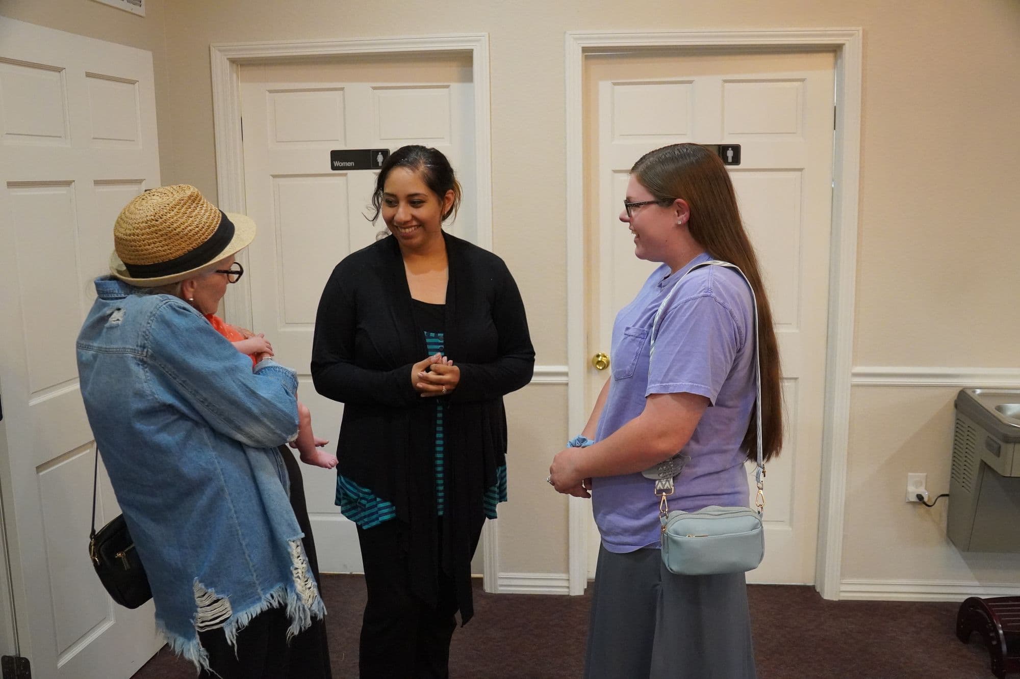 Three women greeting one another and a new baby after worship